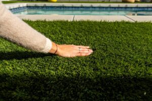 Hand on artificial grass with a pool in the background. 