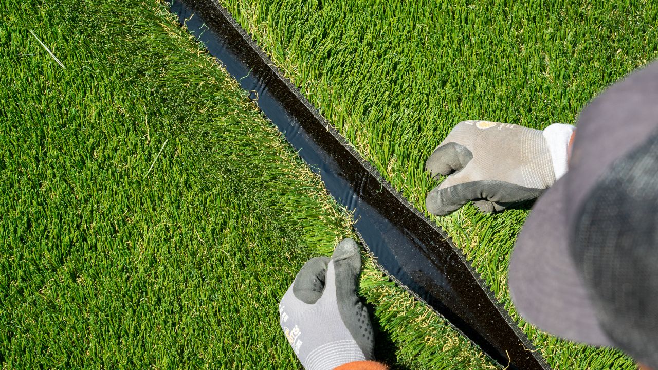 A closeup photo of an artificial grass installer closing the seam on turf