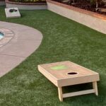 a residential backyard lawn installed by Artificial Turf Supply with a pool and corn hole game